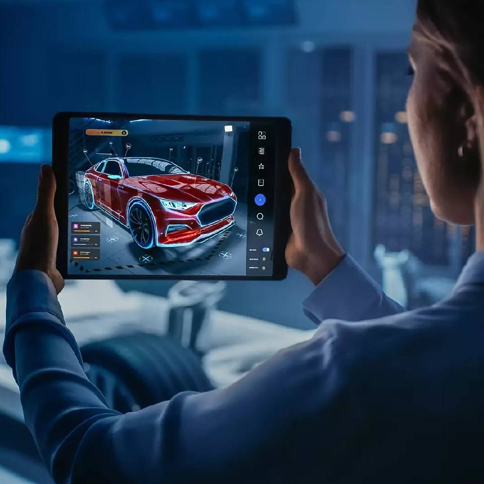 A woman holding a tablet with a car model in a 3D software in front of a car chassis