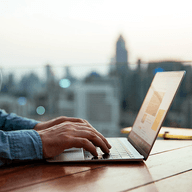 Hands typing on laptop, city skyline.