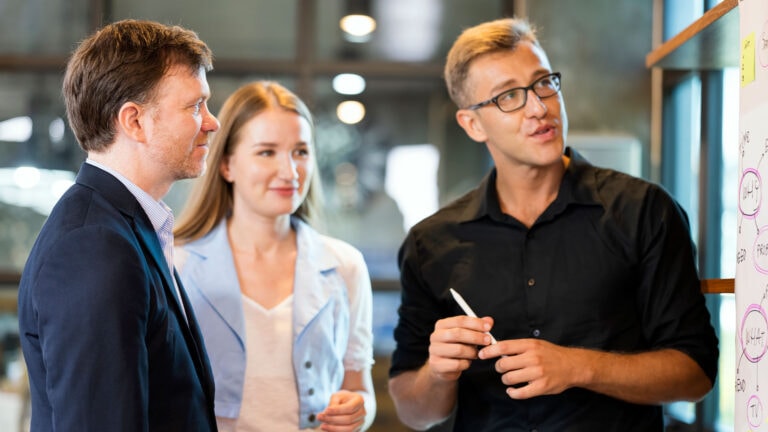 three people talking and looking at a board