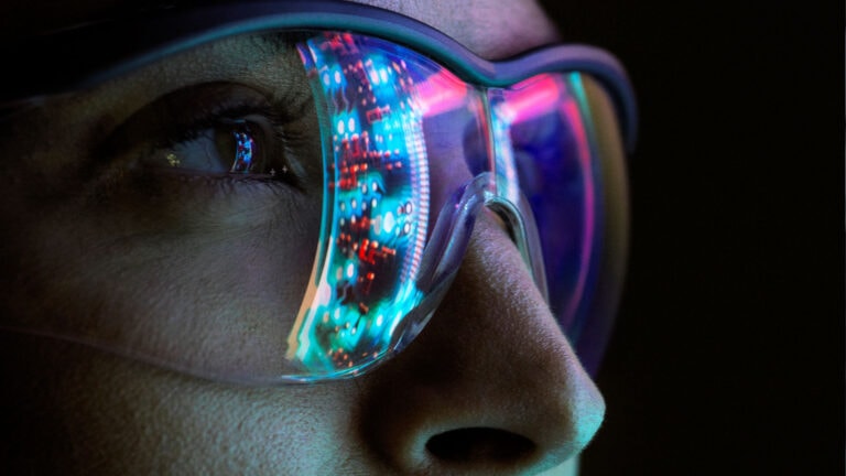 close up view on a woman eyes wearing glasses that relects the lights of a computer bay