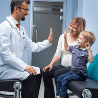 A toddler sitting beside his mom doing high five with a doctor