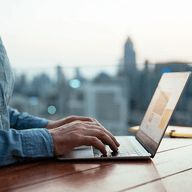 Hands typing on laptop, city skyline.