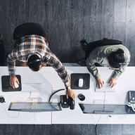 Overhead view of two people working at laptops on a long white desk