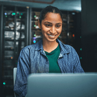 female it technician in a server room and using a laptop