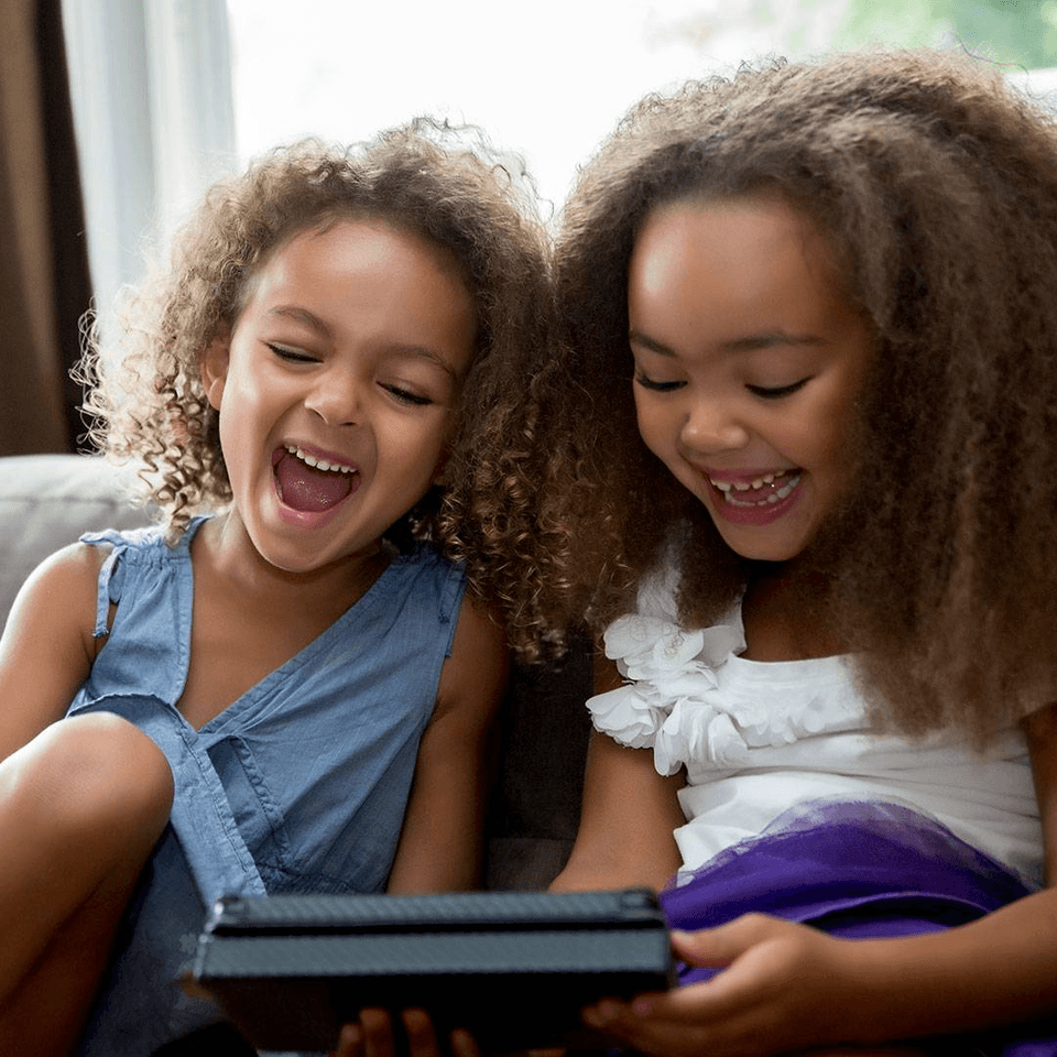 two little girls smiling while looking at a tablet