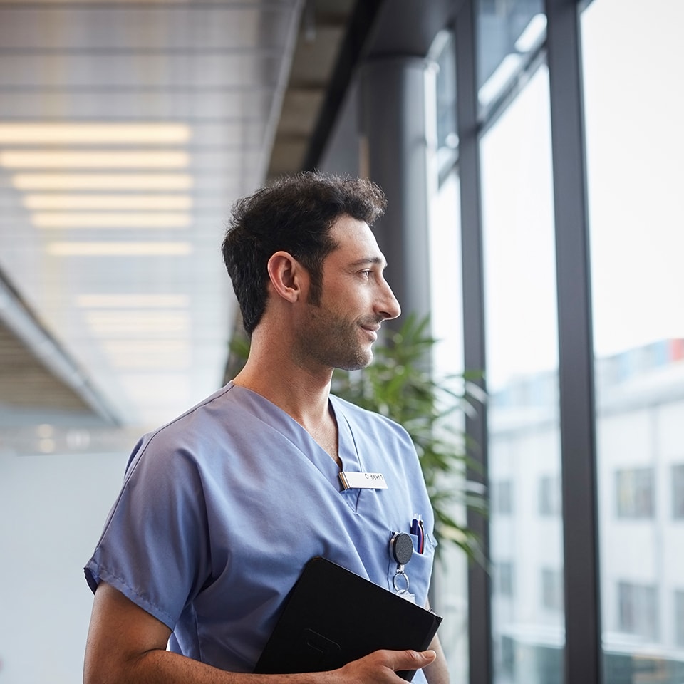 young male nurse holding digital tablet while looking through window at hospital